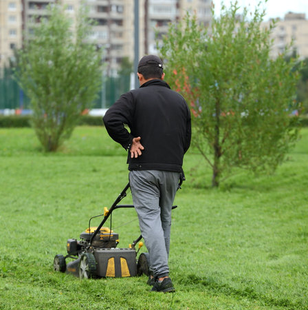 A Park employee mows the grass with a lawn mower, Rossiyskiy prospect, Saint Petersburg, Russia, August 2020のeditorial素材
