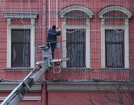A worker hangs holiday garlands on the wall of a house, 176 Nevsky Prospekt, Saint Petersburg, Russia, December 2020のeditorial素材