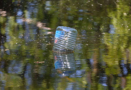 A plastic bottle floats upside down in the murky green waterの写真素材