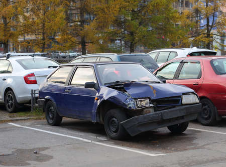 A broken blue passenger car is parked in a street parking lot