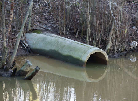 Concrete drain sewer pipe on the Bank of a dirty riverの写真素材