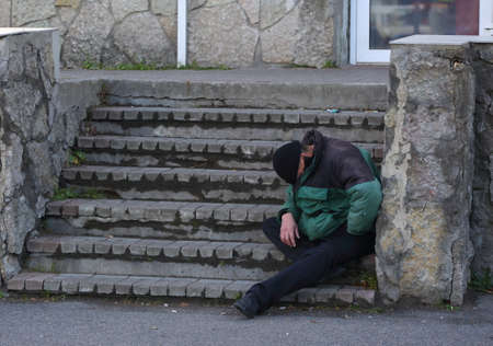 A homeless beggar sleeping sitting on the steps of a stone staircase of a city buildingの写真素材