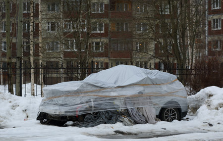 Crashed car covered with polyethylene in the courtyard of a residential buildingの写真素材