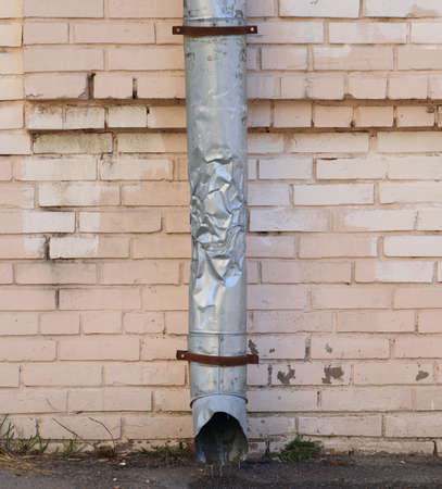 A crumpled gray metal downpipe on a pink brick wall