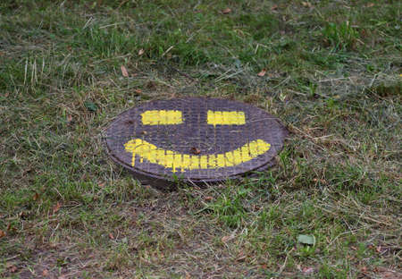 Smiley face painted in yellow paint on a metal manhole coverの写真素材