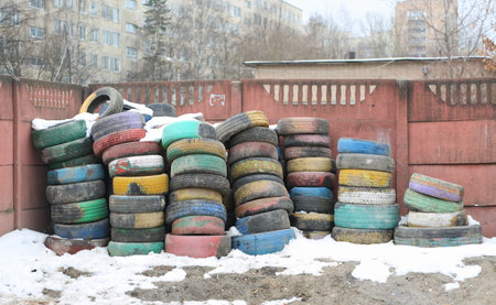 Used multicolored car tires are stacked in piles near a pink concrete fenceの写真素材