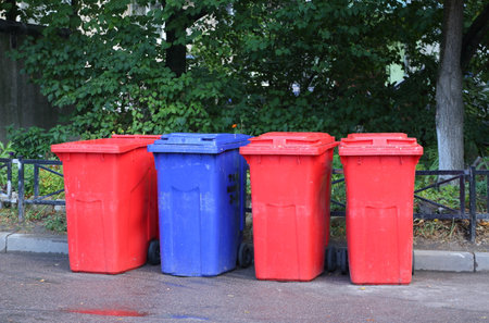 Colored garbage containers stand on the asphalt near the lawnの写真素材