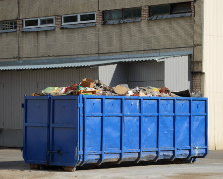 A large metal blue dumpster near the wall of the houseの写真素材