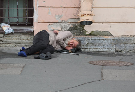 A homeless beggar sleeps on the asphalt near a house wall, Duma Street, Saint Petersburg, Russia, September 18, 2023のeditorial素材