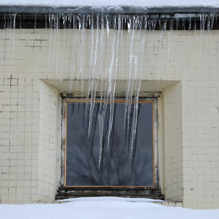 Long icicles hang from the roof in front of the windowの写真素材