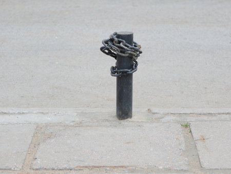 A black metal post driven into the pavement is wrapped with a metal chainの写真素材