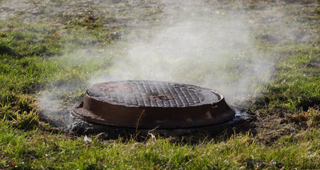 Steam over a round rusty metal manhole in last year's grass
