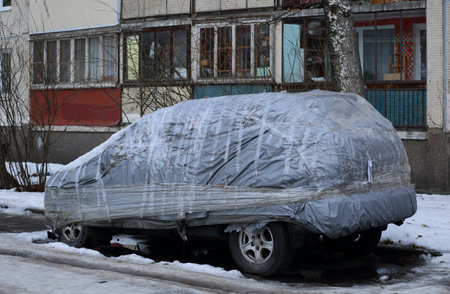 Car covered with a gray cover in the yard of the houseの写真素材
