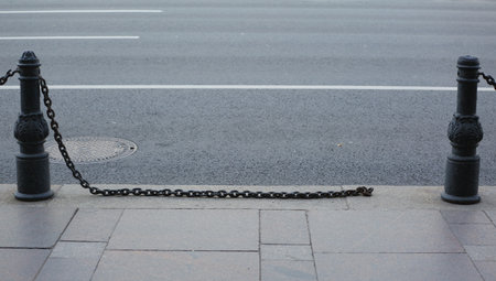 The broken chain of the fence separating the sidewalk and the pavementの写真素材