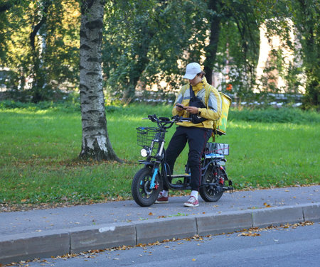 A food delivery courier sits on an electric bikeの写真素材
