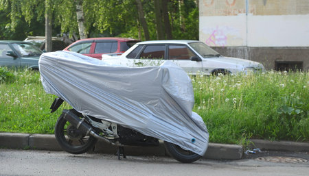 Motorcycle covered with a cover standing near the lawnの写真素材
