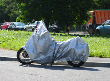 Motorcycle covered with a cover standing near the lawnの写真素材