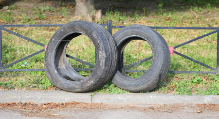 Two old used car tires are standing near the lawn fence
