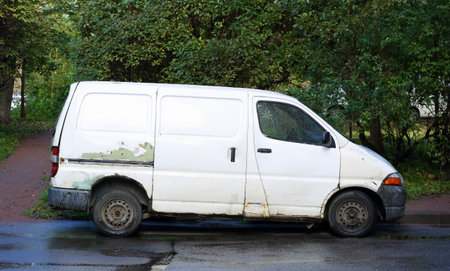 An old, rusty white minivan is parked near a lawn