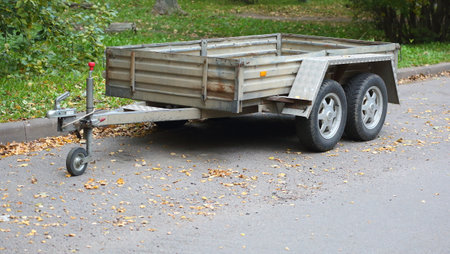 An open gray four-wheel car trailer is parked near a lawn