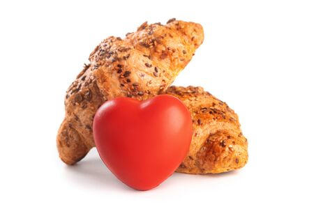 Photo of fresh golden croissants covered sunflower seeds and sesame isolated on white background with red heartの写真素材
