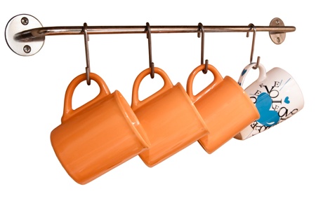 Teacups orange hang on hooks on a white backgroundの写真素材