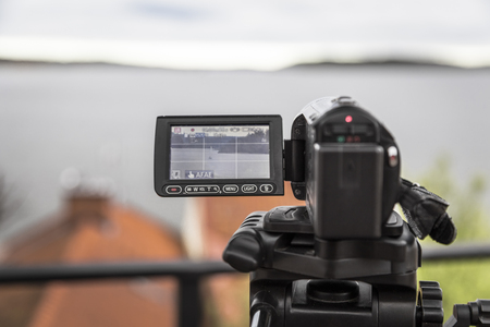 A video camera mounted on a tripod shoots a landscape with a yacht