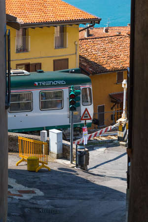 Sale Marazino, Italy-August 29, 2015: railway crossing with a passing train on a narrow street in...