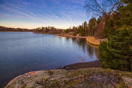 Finland, Helsinki - A picturesque lake in the sunset, a rocky wooded shore with sandy beaches, a...
