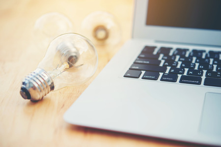 bulb and laptop on wooden tableの写真素材