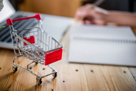 Red shopping cart and laptop on wooden table,shopping online concept.の写真素材