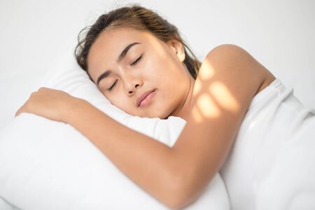 Beautiful young brunette woman sleeping in a white bed.の写真素材