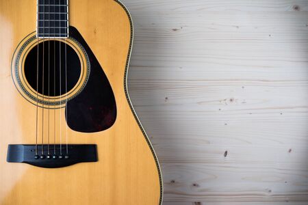 Acoustic guitar resting against a wooden background with copy space