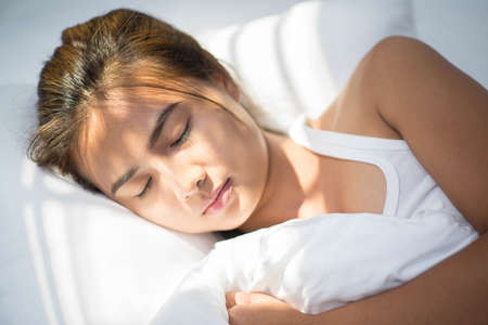 Beautiful young brunette woman sleeping in a white bed.の写真素材