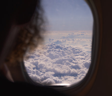 hairstyle with curly hair against the background of cumulus clouds in the airplane window in flight...