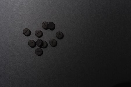 Close up of ten black round pills absorbent carbon lay on a rough grey surfaceの写真素材