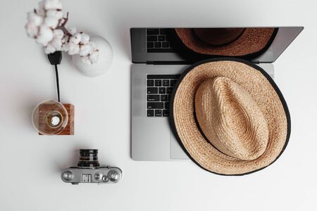 A top view of white vase of cotton flowers on a table, old-fashioned camera, time-worn lamp and vintage straw hat lying on a notebook. Soft and calm concept of old time things with modern electronicsの写真素材