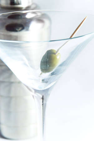 Olive in Martini glass with out-of-focus cocktail shaker in background.  Cocktail shaker image in stem of glass.  [Short depth of field, on white.]の写真素材