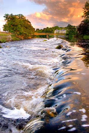 Water running over weir at evening at Grassington, Yorkshire Dales National Park, North Yorkshire, Englandの写真素材