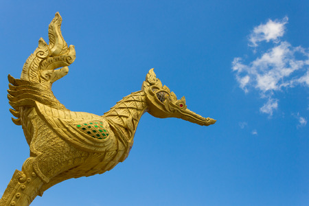 Thai golden swan statue with red eye on blue sky background at corner. Golden swan cement statue in Thai style.の写真素材