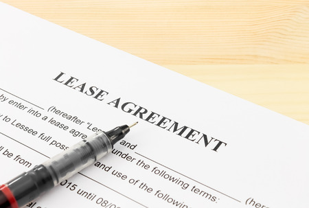 Lease agreement contract sheet and brown pen at bottom left corner on wood table backgroundの写真素材