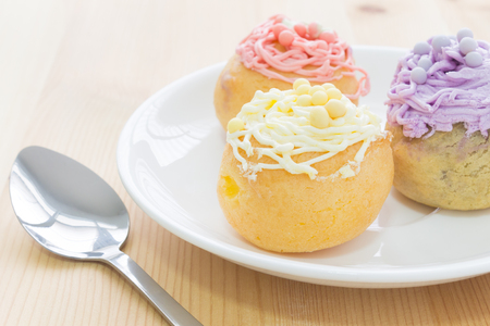 Highlight at yellow choux pastry or cream puff or profiterole that have whipped cream on the head. Eclair dessert in white dish and spoon.の写真素材