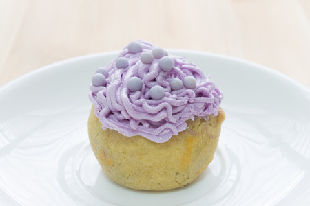 Purple choux pastry or cream puff or profiterole that have whipped cream on the head. Eclair dessert on wood table.の写真素材