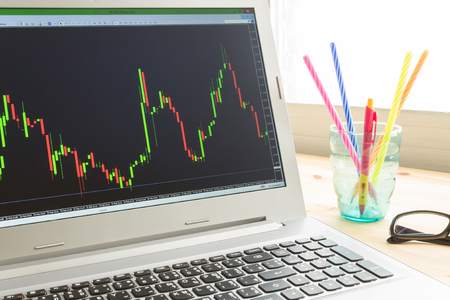 Forex graph or stock graph in laptop screen on wood table and pen and black glasses on left viewの写真素材