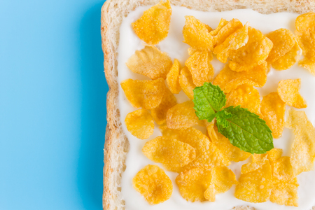 Cornflakes on Yogurt on Bread with Peppermint on Blue Pastel Background Flatlay Close Up. Cereal Breakfast bread healthy clean food for food and dessert categoryの写真素材