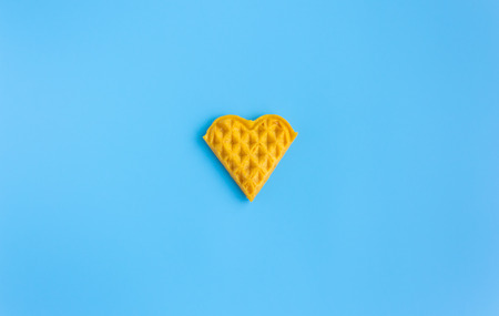 1 Piece Heart Shape Waffle on Blue Pastel Background Minimalist Style Wide Angle. Heart shape waffle dessert in minimalist style for food and dessert categoryの写真素材