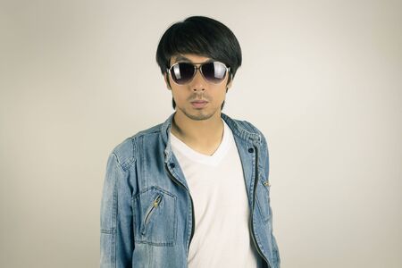 Young Asian Man in Jeans Jacket or Denim Jacket Wear Sunglasses in Front View. Denim or Jeans Jacket Men Fashion on Gray Backgroundの写真素材