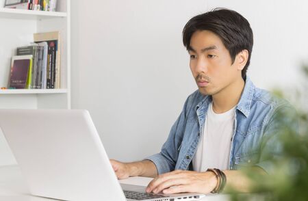 Young Asian Casual Businessman Working with Laptop at Workplace in Home Office. Casual business or informal business in home officeの写真素材