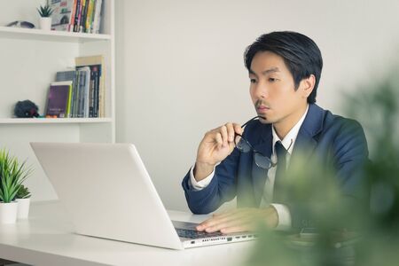Asian Financial Advisor or Asian Consulting Businessman Serious with Financial Information in front of Laptop. Asian financial advisor or Asian consulting businessman working in officeの写真素材