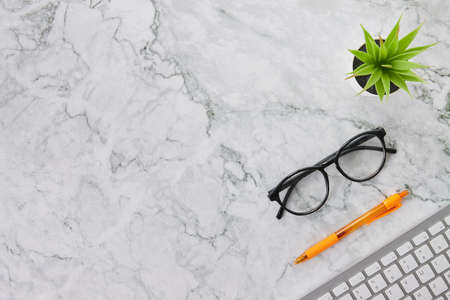 Modern Clean Flat Lay or Top View Office Desk or Office Table and Office Supplies as Computer Keyboard,Pen,Glasses,Office Plants on Marble Minimalist Backgroundの写真素材